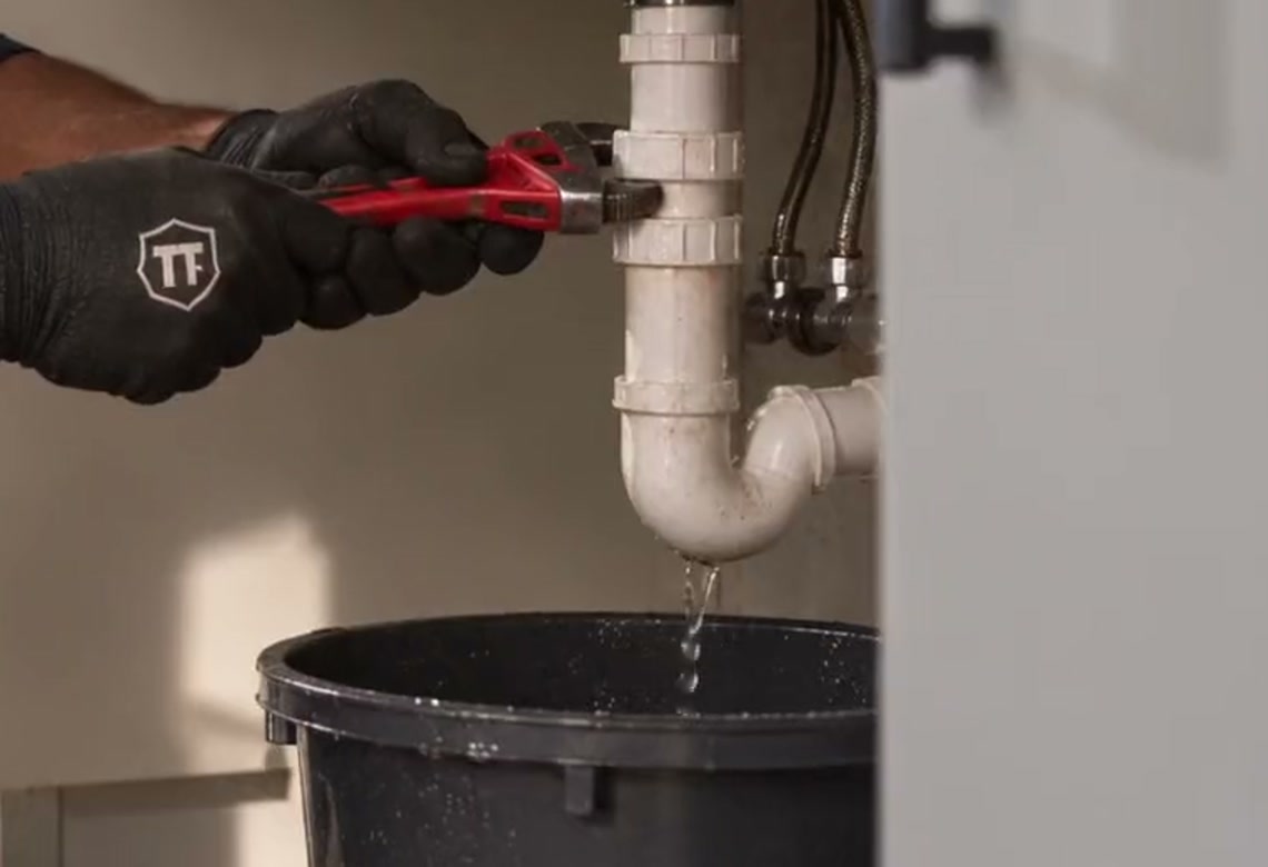 An opened sink trap draining into a bucket